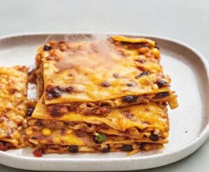 Eine leckere mexikanische Quesadilla-Auflauf mit Schichten aus Rindfleisch, Tortillas, schwarzen Bohnen, Tomaten, Mais, grünen Chilischoten und geschmolzenem Cheddar-Käse, perfekt gebacken.